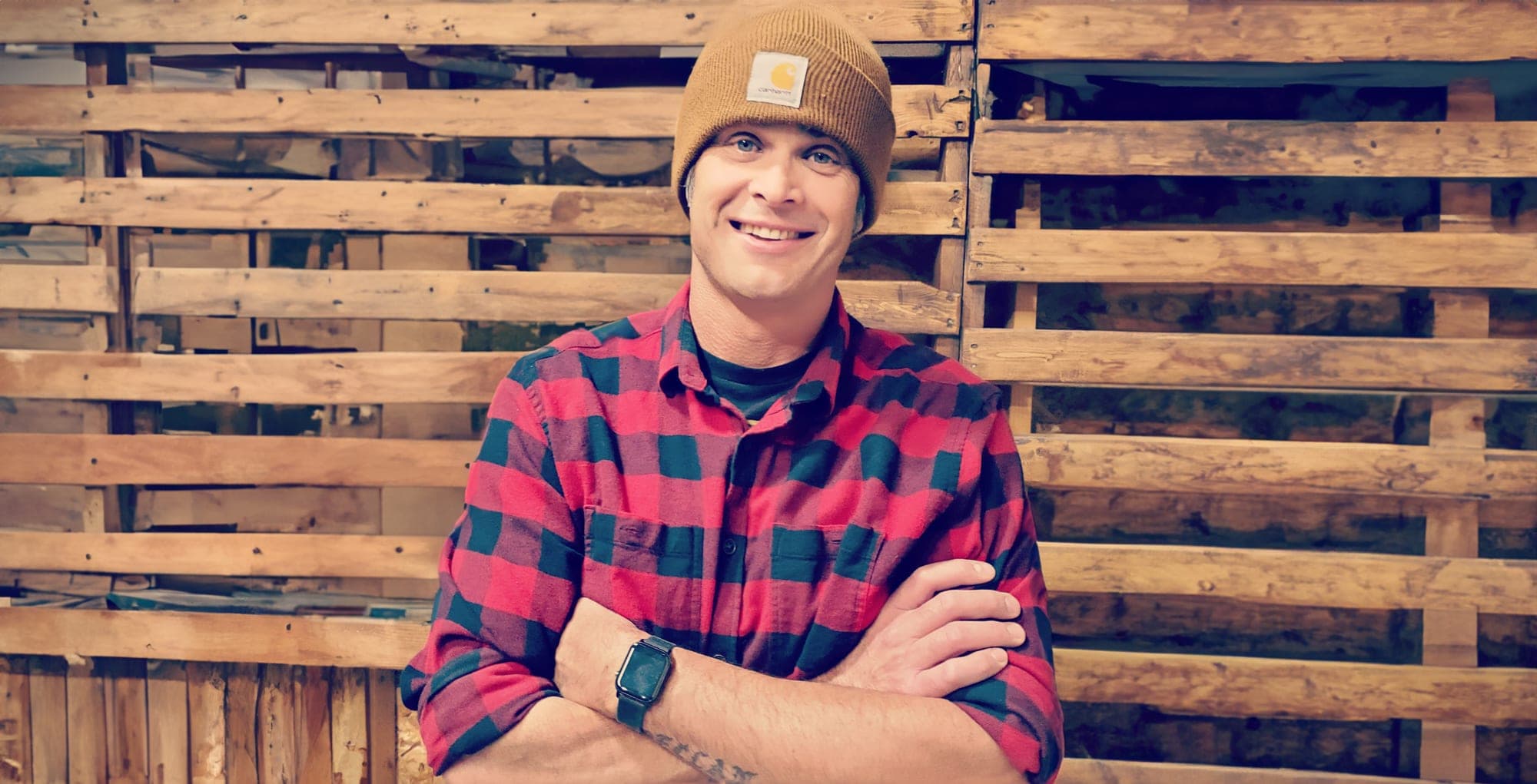 Lee Schindler standing in front of a reclaimed wood wall