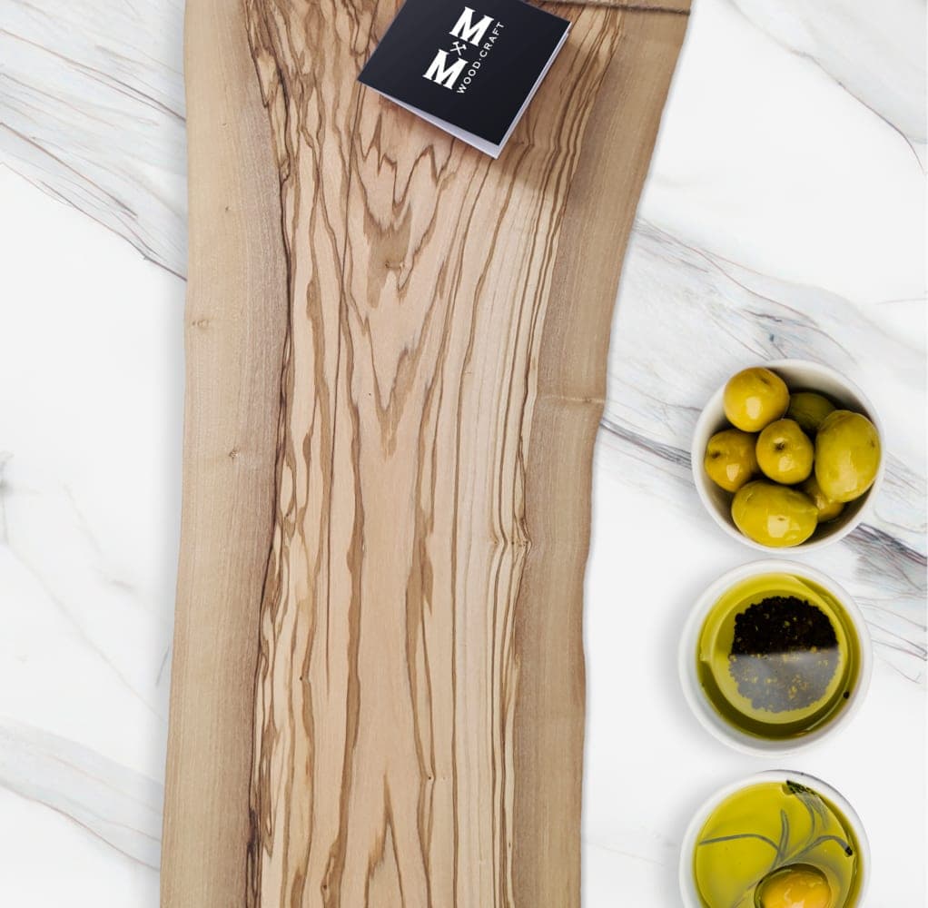 Olive Grove live-edge olive wood charcuterie board on marble with olives and a Moose Mill tag