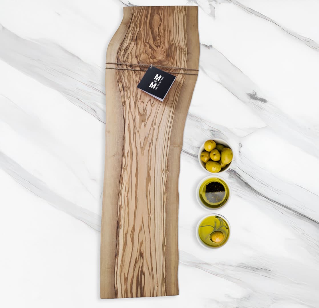 Olive Grove live-edge olive wood charcuterie board on marble with olives and a Moose Mill tag